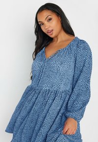 Niebieska sukienka w kropki z długimi puff sleeves, dekoltem w serek i zgromadzonym dołem. Wykonana z lekkiego materiału o gładkiej teksturze i ciemnych kropeczkach.