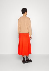 Sudadera marrón claro con textura acanalada combinada con una falda plisada roja vibrante. La modelo lleva botas negras de plataforma con calcetines estampados.