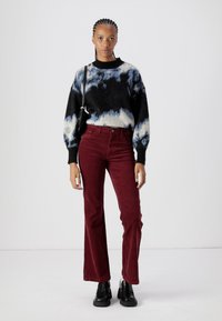 Zwarte sweater met blauw en wit abstract patroon; bordeaux corduroy flared broeken; zwarte laarzen; kleine zwarte schoudertas.