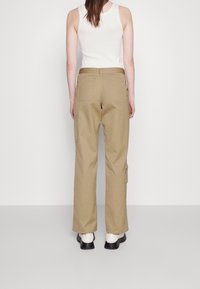 Khaki cargo-housut, joissa on sivutaskut, valmistettu kestävästä kankaasta, suora lahkeensuu ja vyölenkit; yhdistettynä valkoiseen tanktoppiin ja nilkkabootseihin.