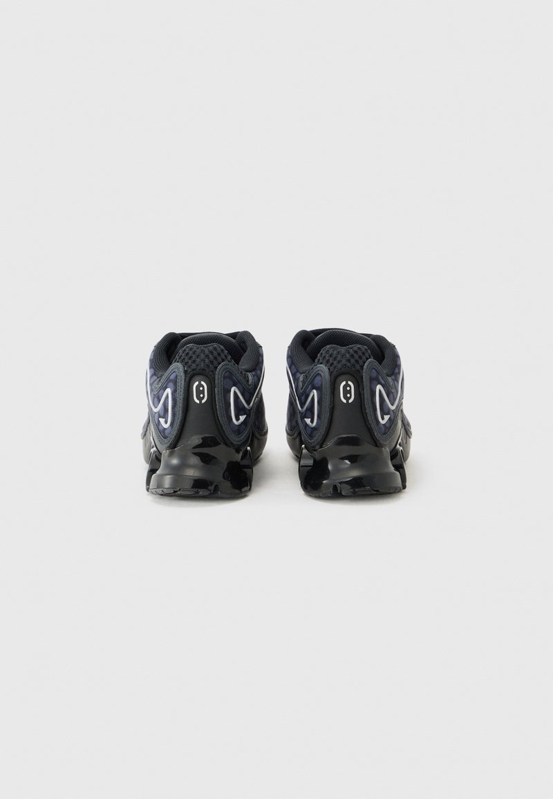 Zapatillas deportivas negras con parte superior de malla y textil, suela gruesa y acentos de diseño ondulado en azul y blanco. Vista trasera que muestra los detalles.