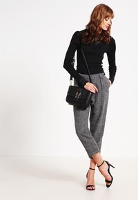 Zwart langetermijn top met kantaccenten, gecombineerd met grijs geruite broek. Het model houdt een gestructureerde zwarte handtas vast en draagt zwarte hakken met bandjes.