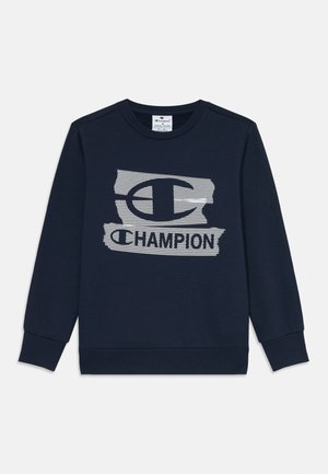 Tumši zils džemperis ar garām piedurknēm, ar teksturētu Champion logo baltā krāsā uz krūtīm un ribētu piedurkņu un apakšmalu.