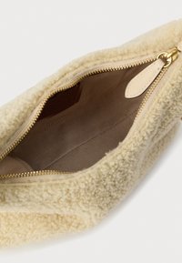 Pūkains bēša krāsas soma ar rāvējslēdzēja aizdari. Iekšpusē mīksta brūna oderējuma. Zelta krāsas metāla detaļas. Mīksta tekstūra ar apaļu formu.