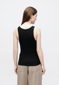 Crni top bez rukava s uskim krojem; mekani materijal; zaobljeni izrez; diskretan detalj logotipa blizu stražnjeg izreza.