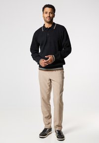 Maglione nero a coste con colletto e polsini a righe in contrasto, abbinato a pantaloni beige e sneakers nere.