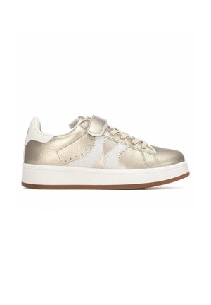 Zapatilla baja metálica dorada con acentos blancos, tira de velcro, cordones y suela blanca gruesa con base marrón, vista lateral sobre fondo blanco.
