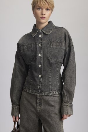 Black denim jacket with visible stitching, spread collar, large chest pockets, and snap buttons, paired with matching denim pants.