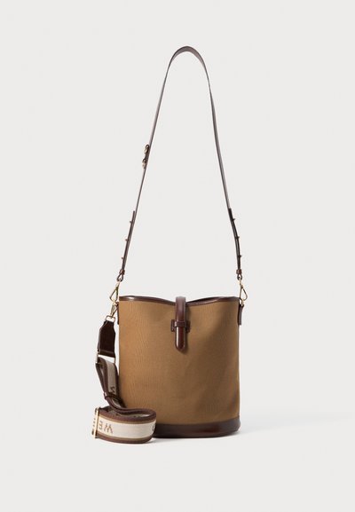 Sac seau en toile marron avec une base en cuir et des accents en cuir. Il est doté une sangle détachable avec un motif tissé et une longueur ajustable.