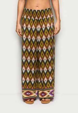 Pantalones de pierna ancha con cintura elástica con un patrón geométrico de diamantes en verde, marrón, púrpura y blanco, combinados con sandalias de plataforma.
