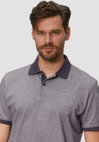 Szary polo z ciemnofioletowym kołnierzykiem. Ma wyszyty tekst na klatce piersiowej oraz miękką teksturę. Klasyczny krój, krótki rękaw.