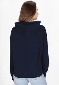 Hanorac cu glugă de culoare albastru marin, cu un croi lejer, manșete și tiv cu nervuri. Textură fină și detalii minime pentru un design simplu.