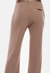 Pantaloni larghi beige con una texture di tessuto liscia. Dotati di una vita in satin e una singola tasca posteriore con rifinitura in satin.