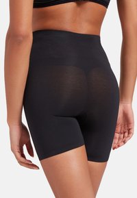 Hooggesneden knielange zwarte shapewear van soepel, rekbaar materiaal, met een naadloos ontwerp en een discreet uitsnijding voor gemak.