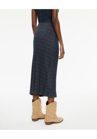 Vestido de punto ajustado de longitud media en color azul marino con un dobladillo en abertura; combinado con botas de estilo western en un tono marrón claro que presentan un bordado intrincado.