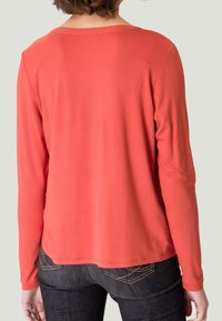 Haut à manches longues en tissu corail, avec un col rond et une texture lisse, porté avec un jean en denim foncé, montrant la vue de dos.
