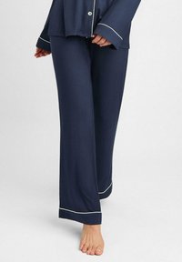 Granatowy zestaw piżamowy z guzikiem u góry i szerokimi spodniami, z białym obszyciem na krawędziach. Miękka, gładka tekstura materiału.