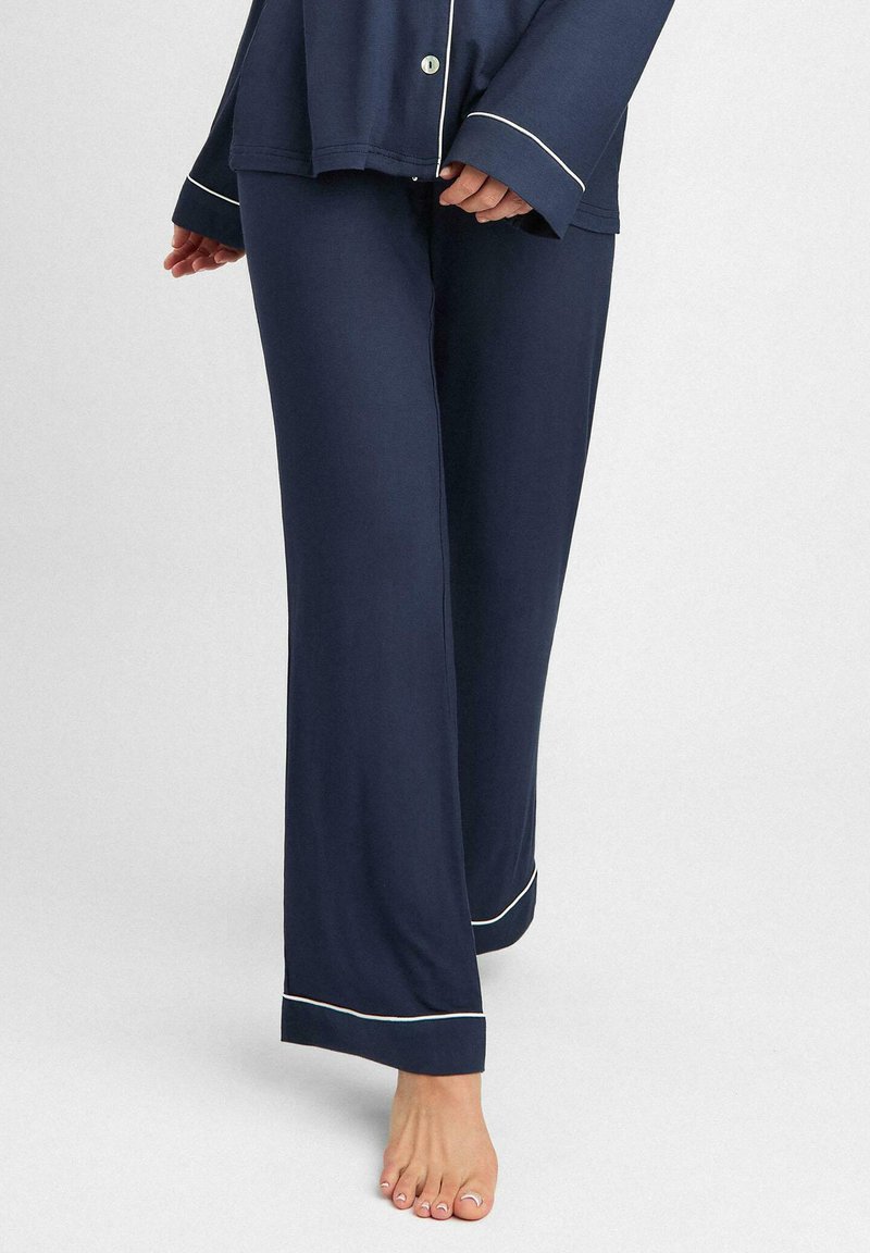 Granatowy zestaw piżamowy z guzikiem u góry i szerokimi spodniami, z białym obszyciem na krawędziach. Miękka, gładka tekstura materiału.