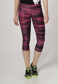 Leggings capri aderenti con un motivo a righe nere e rosa, realizzati in materiale elasticizzato. Abbinati a scarpe sportive nere e verde neon.