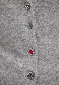 Šedý vlněný cardigan se čtyřmi knoflíky: jeden šedý, dva zdobené kamínky (červené a zelené) a dekorativní černý květinový knoflík.