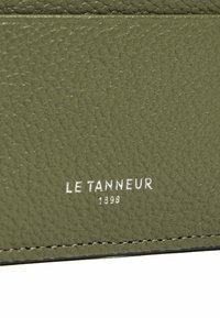 Portafoglio in pelle verde olivo con superficie texturizzata, presenta il logo in rilievo "LE TANNEUR 1898" in argento e dettagli di cucitura sui bordi.