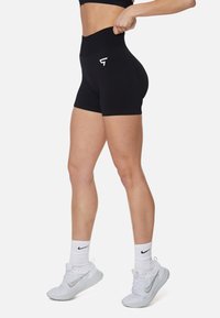 Pantalones cortos deportivos negros de cintura alta hechos de tejido elástico, con un logo blanco y una entrepierna que llega a mitad del muslo.