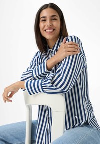 Blauw-wit gestreepte lange mouwen shirt met een button-down kraag, met knopen aan de manchetten, gedragen met lichtblauwe jeans.
