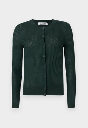 Grønn ribbestrikket cardigan med rund halslinning, lange ermer og knappeåpning med en liten logo foran. Lett stoff.