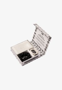 Conjunto de regalo que incluye una bolsa de seda blanca y gomas de pelo en blanco y negro, presentado en una caja decorativa con diseño floral y logo.