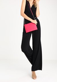 Black jumpsuit with a deep V-neck, loose fit, paired with a pink crossbody bag and nude heels. Smooth texture and modern design.
