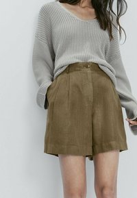 Light gray knit sweater with a V-neck and loose fit paired with high-waisted khaki linen shorts featuring a front button and pleats.