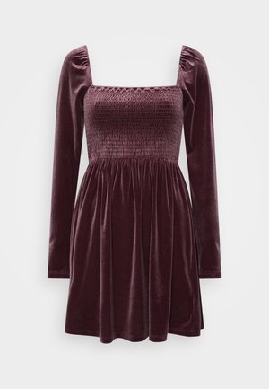 Vestido de terciopelo en un burdeos profundo con escote cuadrado, mangas largas abullonadas, cuerpo fruncido y falda acampanada. Acabado texturizado y suave.