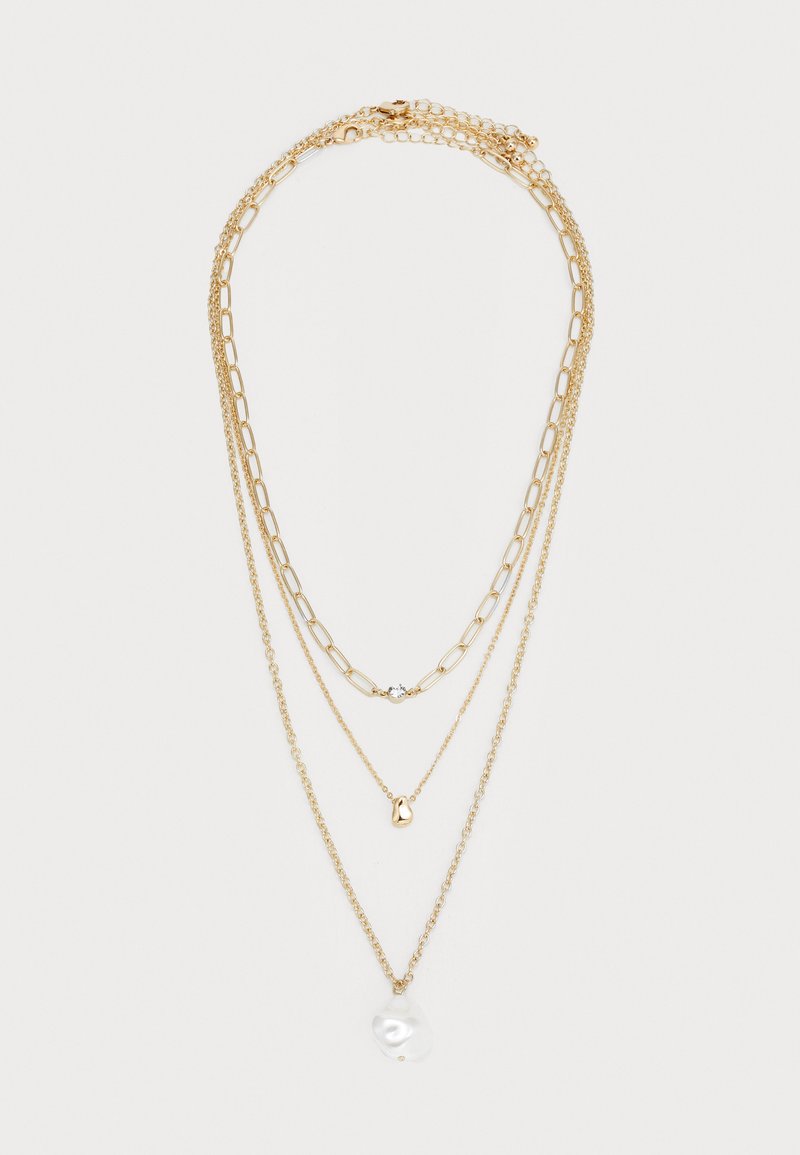 Trojvrstvový zlatý náhrdelník s rôznymi štýlmi reťazí, ktorý obsahuje malý priehľadný drahokam, abstraktný zlatý prívesok a veľký biely perlový prívesok.