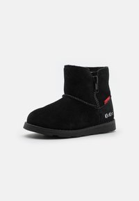 Bottine en suede noir avec une fermeture éclair sur le côté, bout arrondi, surface texturée et semelle en caoutchouc avec un petit logo blanc sur le talon.