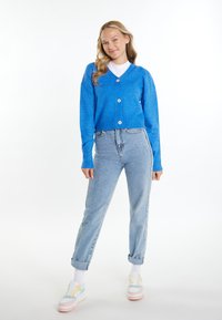 Cardigan blu lavorato a maglia con maniche lunghe e scollatura a V, abbinato a jeans in denim chiaro a vita alta e sneakers multicolore.
