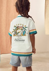 White polo shirt with colorful stripes, featuring a dinosaur graphic and text on the back; paired with denim shorts, smooth texture.