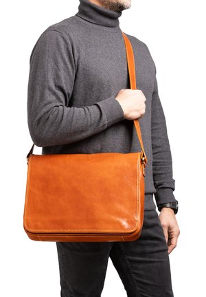 Borsa a tracolla in pelle marrone con una texture liscia, tracolla regolabile e forma rettangolare, presentata con un maglione a collo alto grigio.