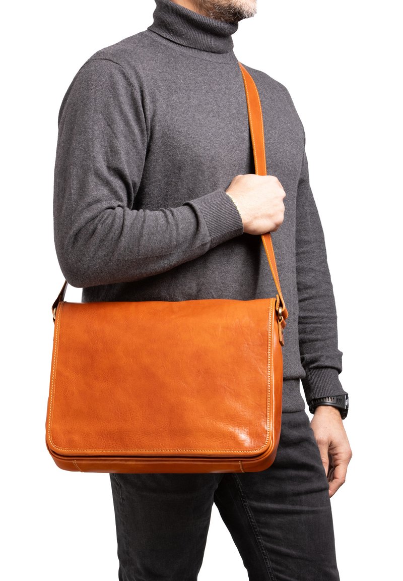 Borsa a tracolla in pelle marrone con una texture liscia, tracolla regolabile e forma rettangolare, presentata con un maglione a collo alto grigio.