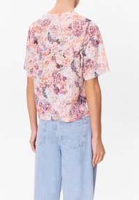 Košile s krátkým rukávem, volného střihu v pastelových barvách s květinovými vzory. Měkká látka, kulatý výstřih a detail na zadním přehybu. Spárovaná se světle modrými džíny.