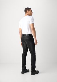 Mustat farkut slim fit -mallisina, joissa on takataskut ja brändätty vyötärönauha, yhdistettynä yksinkertaiseen valkoiseen t-paitaan ja mustiin kenkiin.