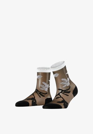 Durchsichtige Knöchelsocken mit schwarzer Spitze und Ferse, weißen Bündchen und schwarz-weißen Blumenmustern auf braunem Hintergrund.