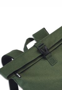 Sac à dos en toile verte avec un design à rabat, fermeture robuste à boucle noire, bretelles réglables et finition en tissu texturé.