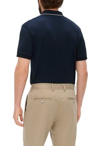 Granatowa koszulka polo z krótkim rękawem, z klasycznym kołnierzykiem i białymi lamówkami. Połączona z beżowymi spodniami stretch, z widocznymi tylnymi kieszeniami.