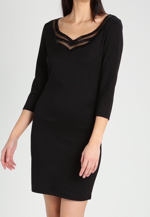 Femme portant une robe noire ajustée avec des manches trois-quarts et un décolleté en V accentué par deux bandes en maille transparente.