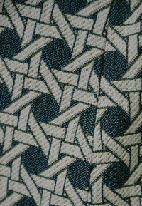 Tkanina tekstylna z plecionym wzorem w kolorze kremowym, granatowym i jasnoniebieskim, tworząca teksturowany, geometryczny design z zazębiającymi się kształtami.