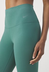 Sportowe legginsy z wysokim stanem w ciemnym odcieniu niebieskiego. Wykonane z gładkiego, elastycznego materiału z szarym logo Nike na pasku.  