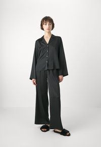 Svart satin pyjamas set som består av en skjorta med knappar och krage samt vida byxor. Tyget har en mjuk textur, kompletterat med fluffiga svarta tofflor.