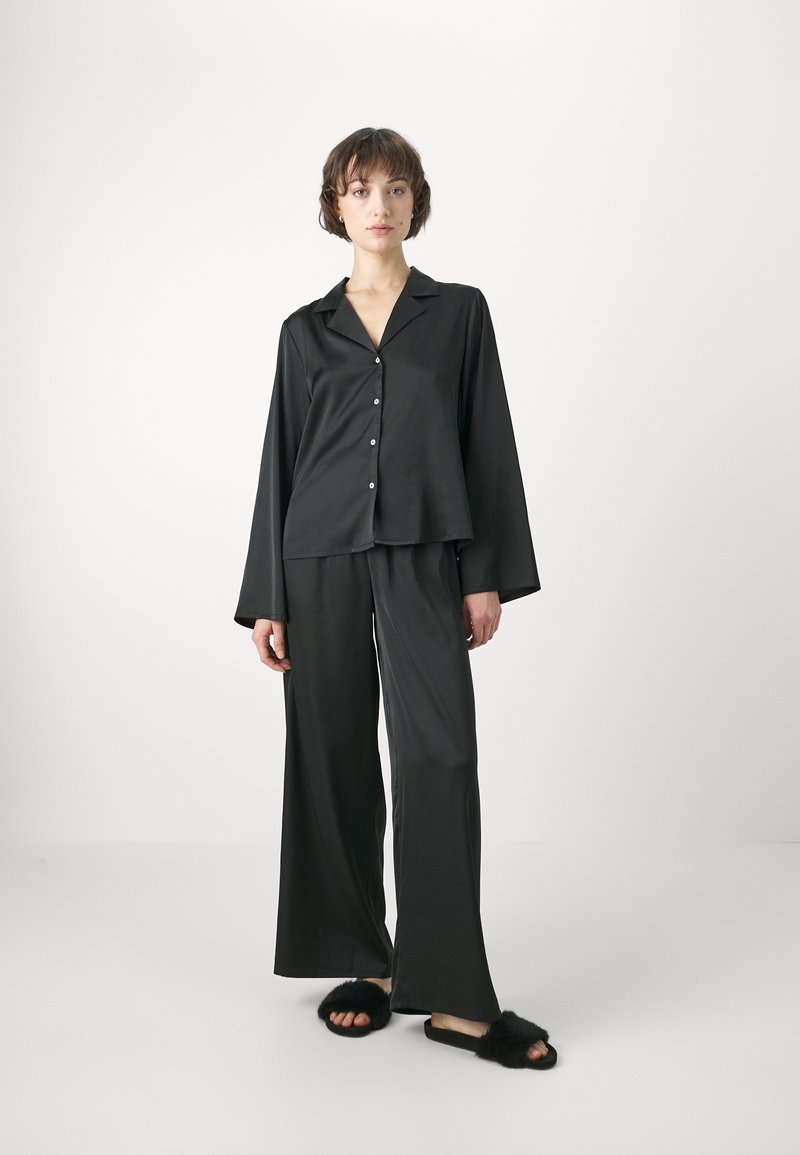 Svart satin pyjamas set som består av en skjorta med knappar och krage samt vida byxor. Tyget har en mjuk textur, kompletterat med fluffiga svarta tofflor.