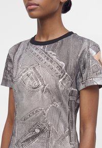 Γυναίκα που φοράει κοντομάνικο t-shirt με μαύρη λαιμόκοψη και ρεαλιστικό τύπωμα ραμμένων τζιν και τσεπών.
