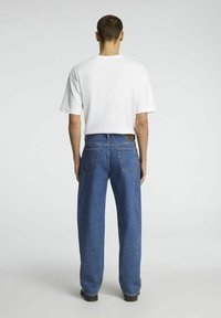 Vit t-shirt kombinerad med blå denimjeans, med rak skärning, klassiska bakfickor och en läderetikett på midjebandet.
